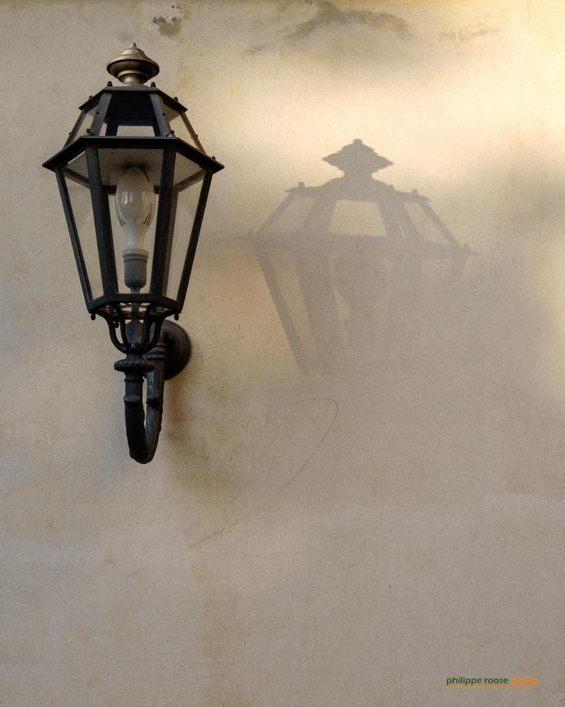 A vintage wall-mounted lantern casting a shadow on a textured wall.